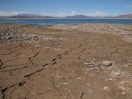 Dry and cracked earth is shown in the foreground with water shown in the distance.