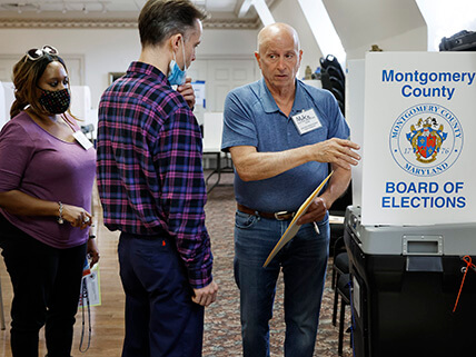 An African American woman is having a conversation with two white men next to a voting booth.