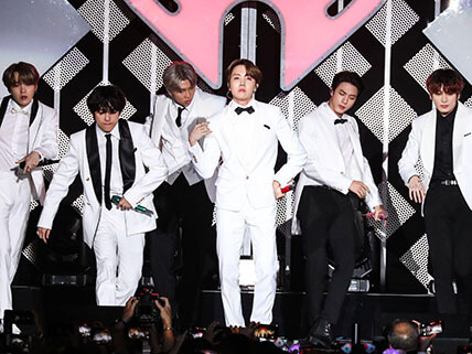BTS in white suits performing on stage.