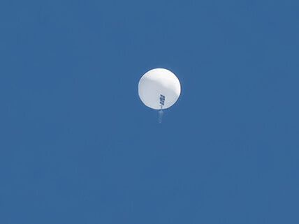 A giant balloon with equipmet hanging from it is visible against a clear sky.